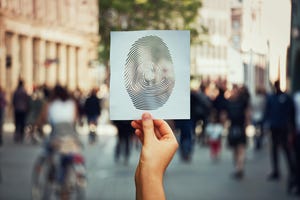 hand holding a paper sheet with fingerprint icon over a crowded street background